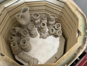 Student pottery pieces inside a kiln at The Pottery Outpost studio in San Diego, showcasing handmade mugs and vases.