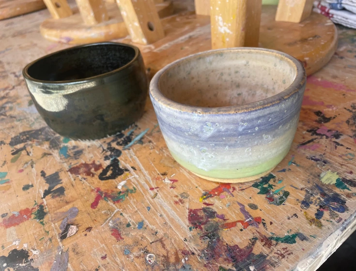 Two finished ceramic bowls on a paint-splattered work table at The Pottery Outpost, created by a beginner pottery student.